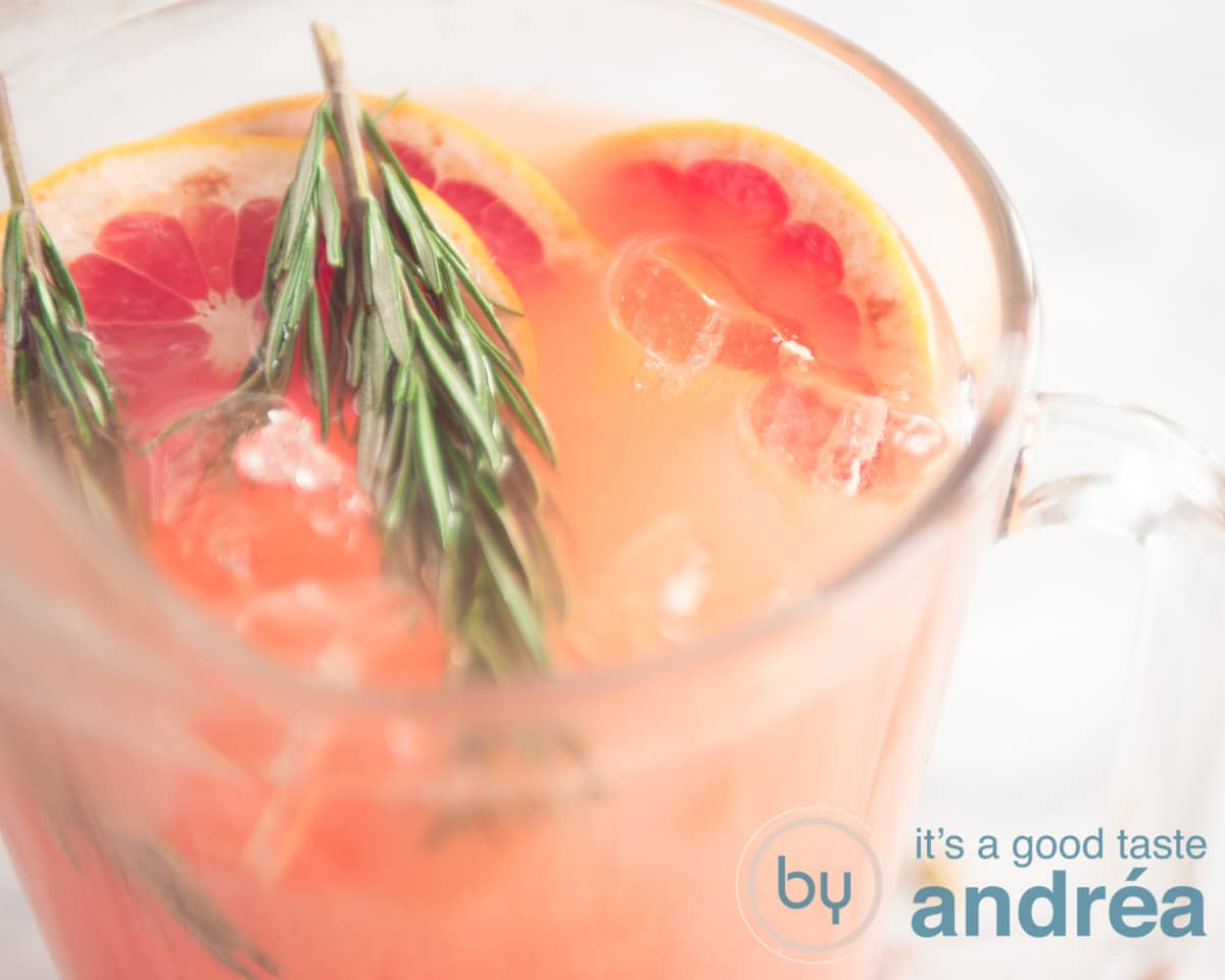 Een kan met rozemarijn grapefruit cocktail gegarneerd met rozemarijn ijsblokjes en grapefruit