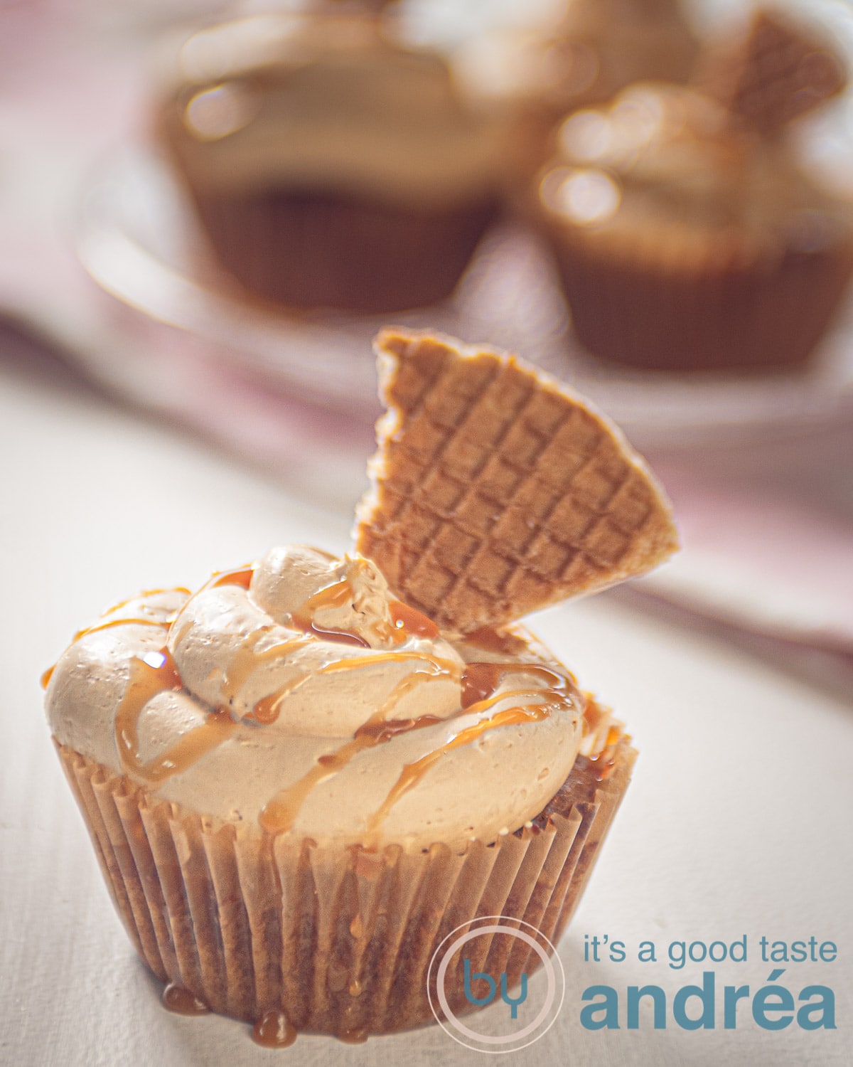Een stroopwafelcake met stroopwafel op de voorgrond op de achtergrond een aantal cupcakes