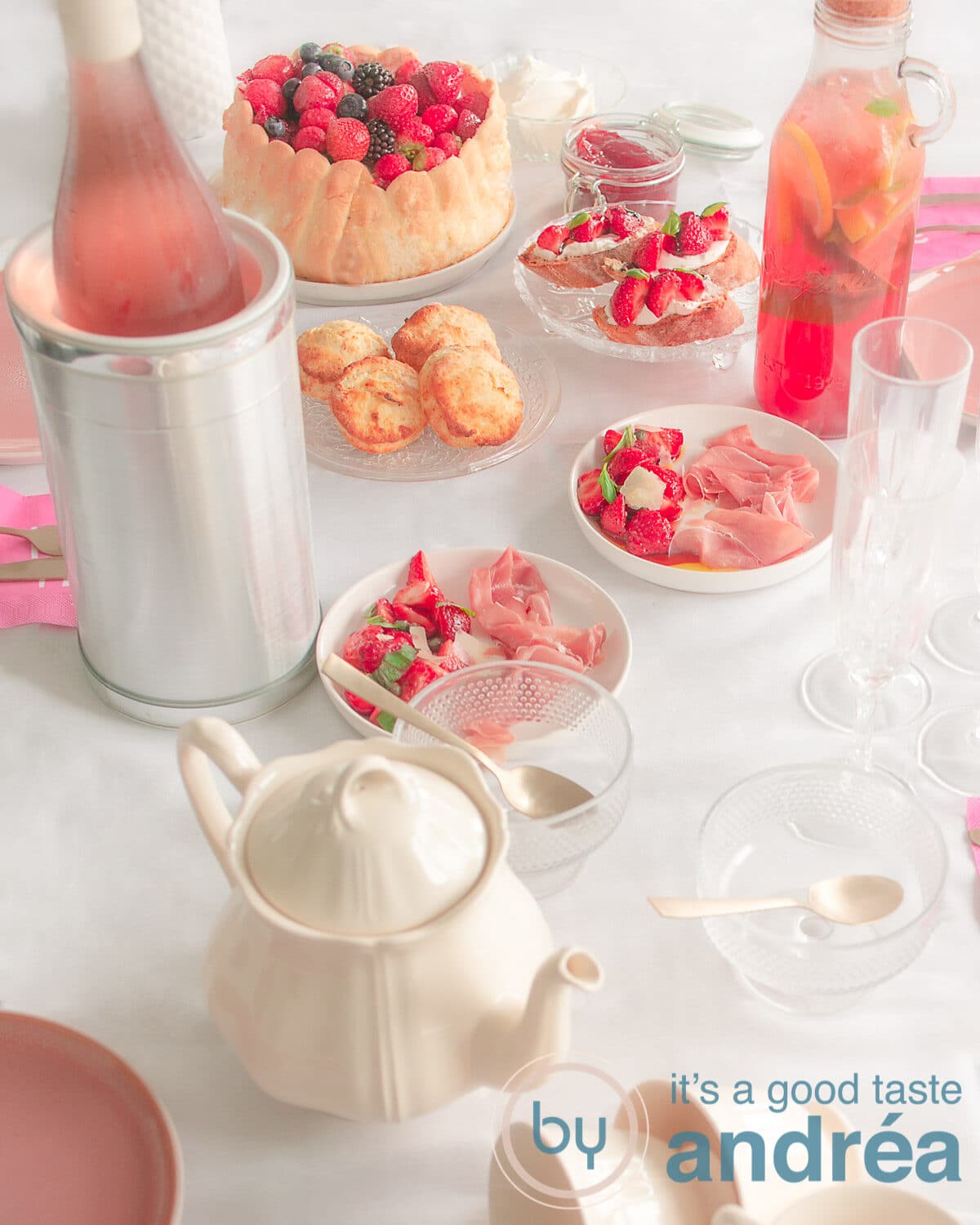a table with recipes for a summer high tea with strawberries, including a tea pot, wine and lots of strawberreis