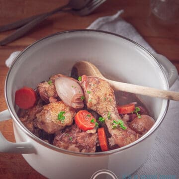 een witte pan met coq au vin op een houten plank