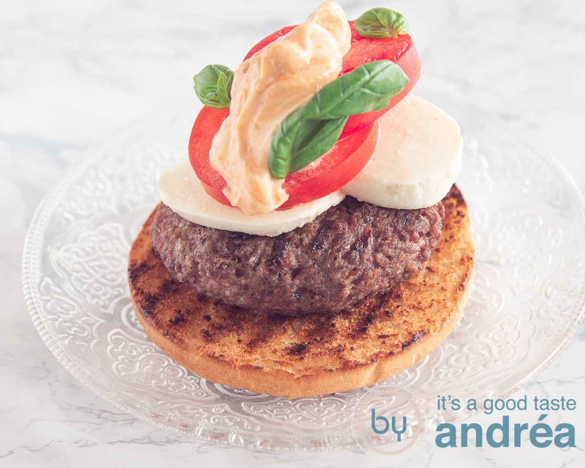 een broodje met een hamburger, mozzarella, tomaat, pesto mayonaise en basilicum blaadjes
