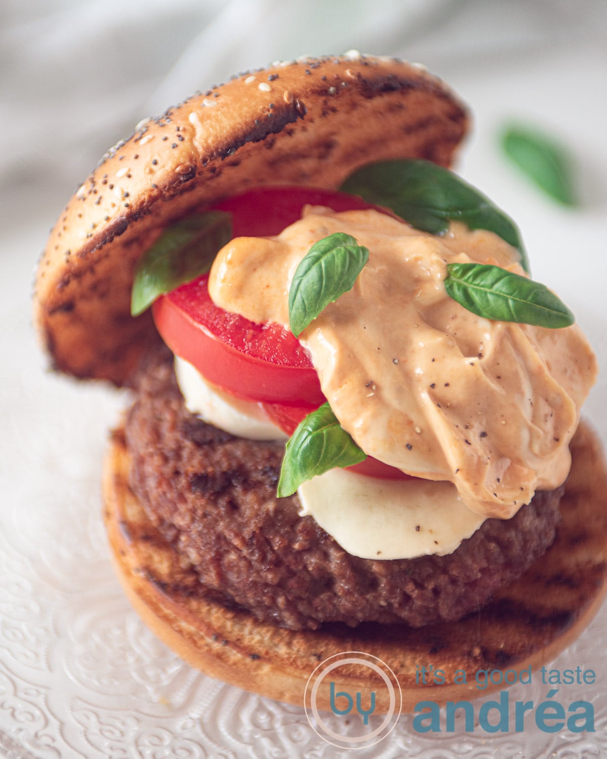 Op een glazen bord een broodje met een burger, Mozzarella, tomaat, pesto mayonaise en basilicum