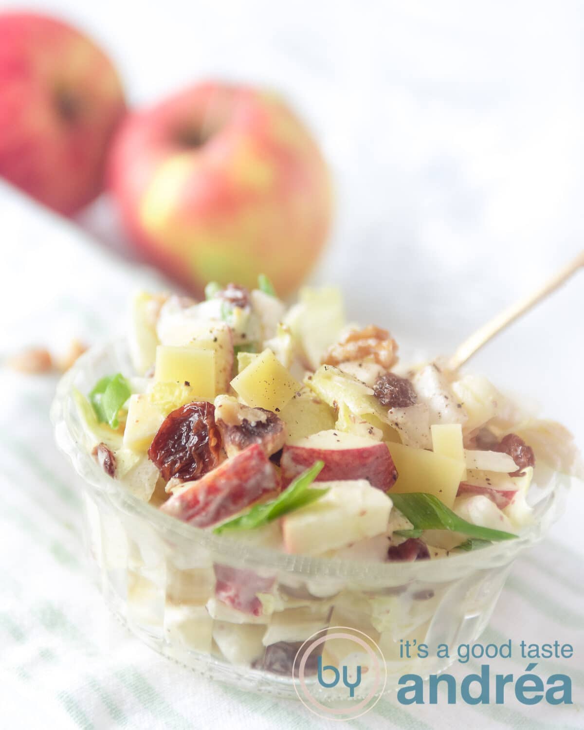 Een schaaltje gevuld met witlofsalade met appel, walnoten, rozijnen. Appels in de achtergrond