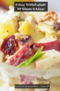 Close-up van witlofsalade met appel, walnoten, rozijnen en kaasblokjes in een romige dressing, geserveerd in een glazen schaaltje.
