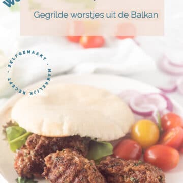 Een wit bord met cevapcici, pita broodjes en groenten