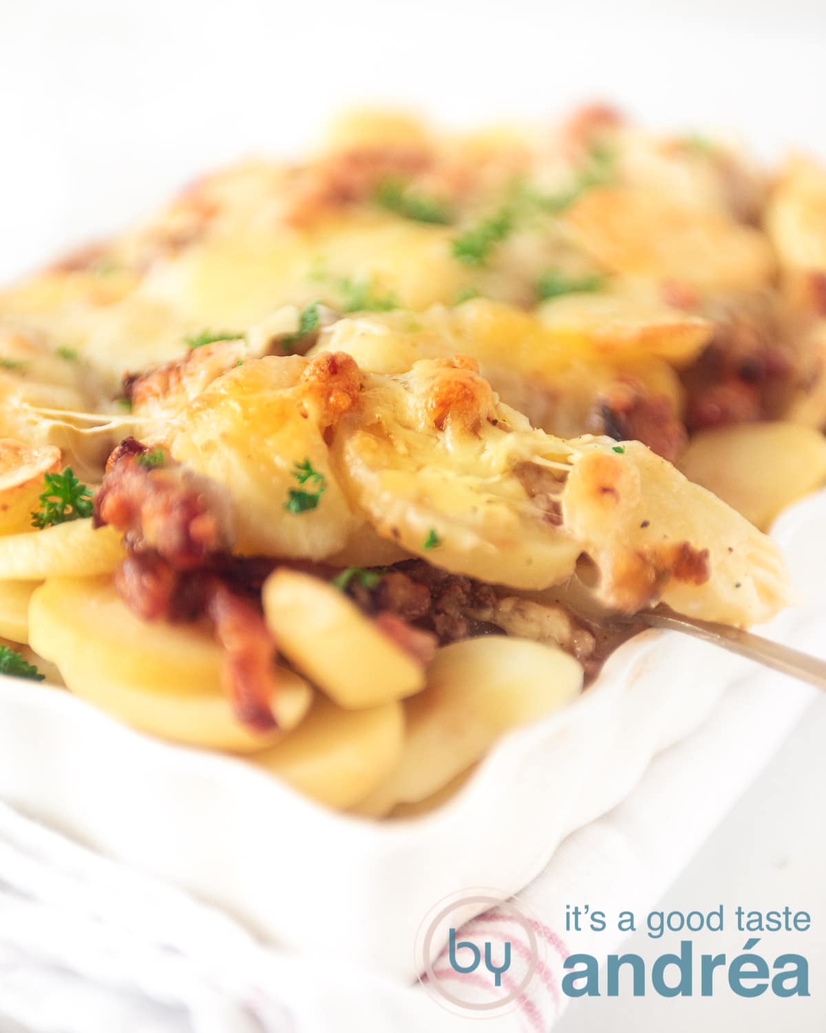 Een lepel pakt een hap aardappel anders uit de ovenschaal.