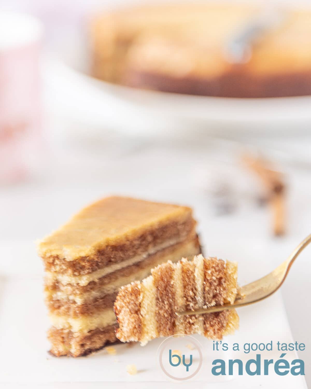 Een vork die een hapje spekkoek vastheeft. Op de achtergrond een plakje spekkoek en de hele spekkoek