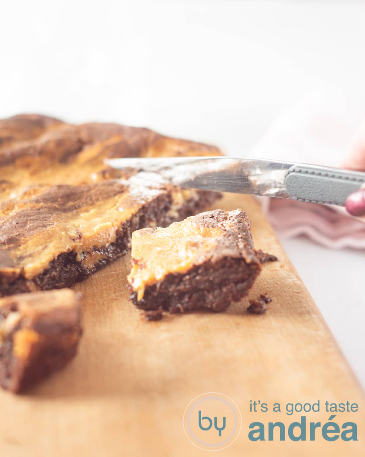 Een hand die blokjes brownie snijdt. De Brownie ligt op een houten plank