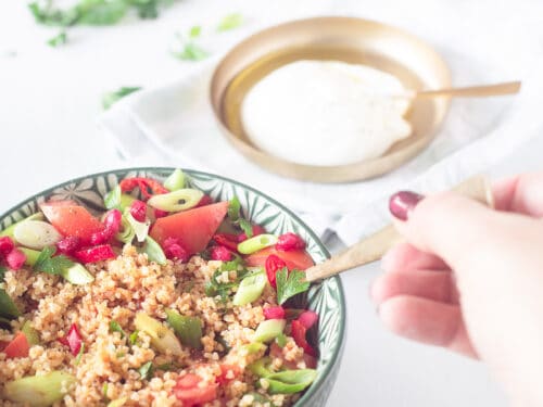 Een heerlijke Kisir salade van bovenaf in een groene schaal een hand neemt een hapje. In de achtergrond een crème Friache dip en wat garnering.