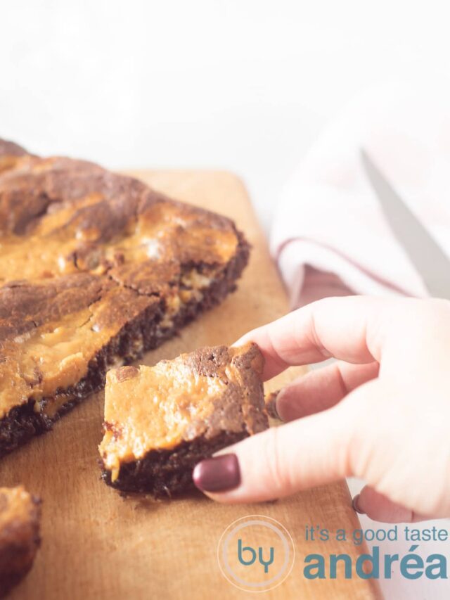Een hand pakt een stukje karamelbrownie van een houten plank