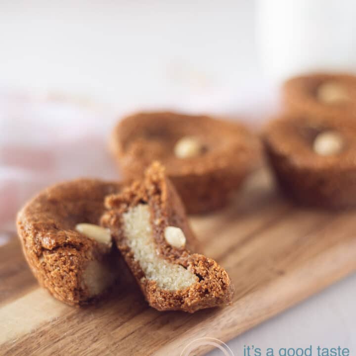 een houten bord met speculaaskoekjes gevuld met Nederlandse amandelen op een witte ondergrond. Een koekje wordt in tweeën gesneden