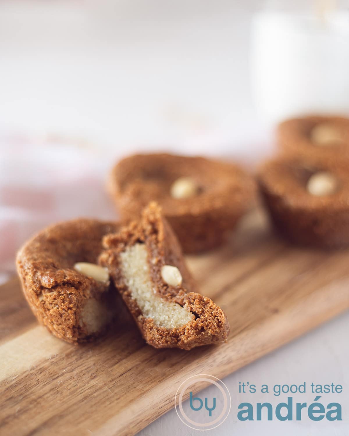 een houten bord met speculaaskoekjes gevuld met Nederlandse amandelen op een witte ondergrond. Een koekje wordt in tweeën gesneden