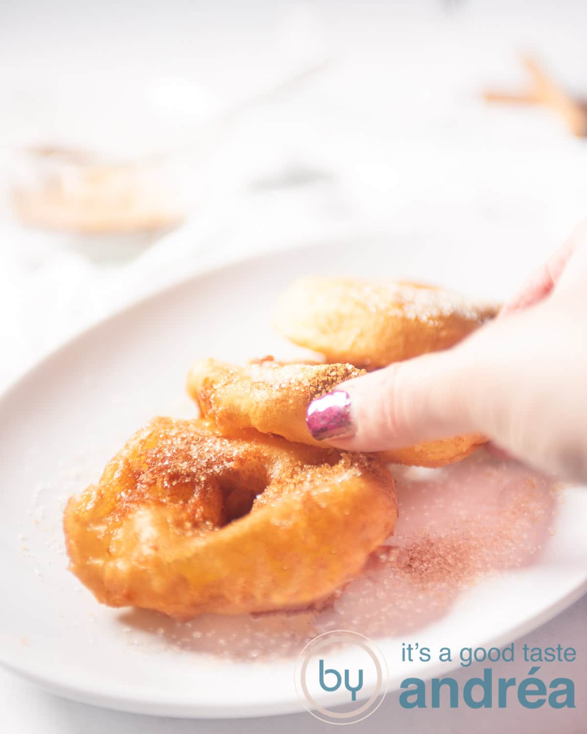 Een hand die een appelbeignet van een witte schaal met drie beignets pakt