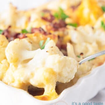 Een witte ovenschaal met daarin bloemkool gratin met spekjes. Een lepel pakt een hap van de bloemkool uit de schaal.