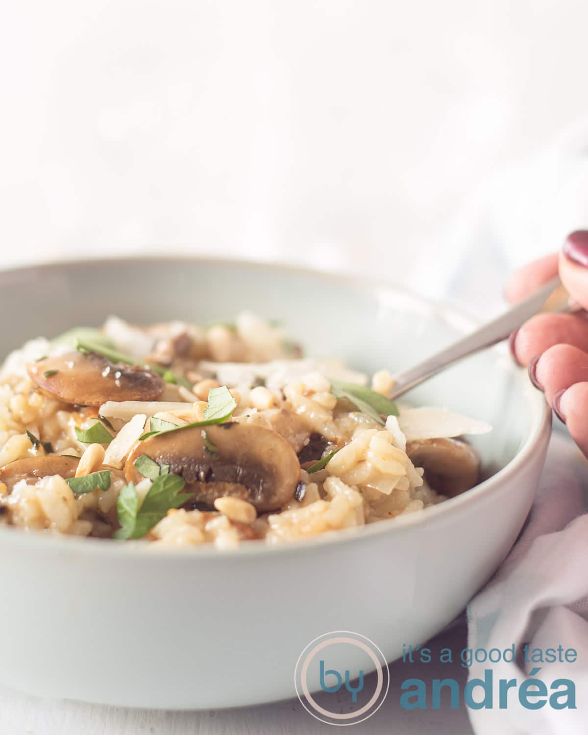 Een schaal gevuld met risotto met kastanjechampignons, een gouden lepel pakt een hapje. Een witte achtergrond