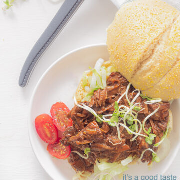 Een foto van bovenaf van een broodje met daarop shredded beef, tomaten en cress. Een witte achtergrond. Bovenin een mes met een grijs handvat
