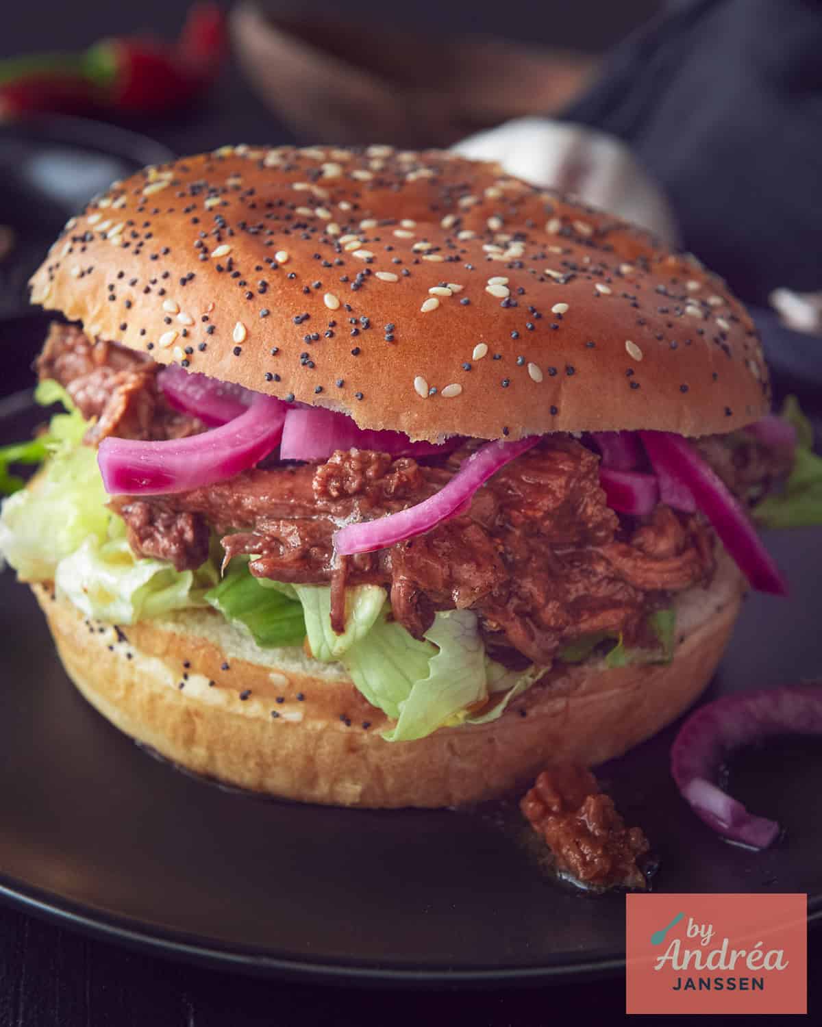 A picture with a bun filled with pulled beef, lettuce and onions on a black background