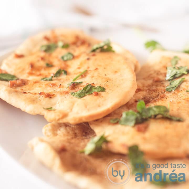 Een vierkante foto met drie naan broodjes met knoflook peterselie boter op een wit dienblad op een witte ondergrond