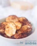 Een bakje vol met chips van courgette gegratineerd met parmezaanse kaas. Op de achtergrond ligt Parmezaanse kaas en een rasp