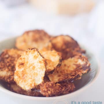 Een bakje vol met chips van courgette gegratineerd met parmezaanse kaas. Op de achtergrond ligt Parmezaanse kaas en een rasp