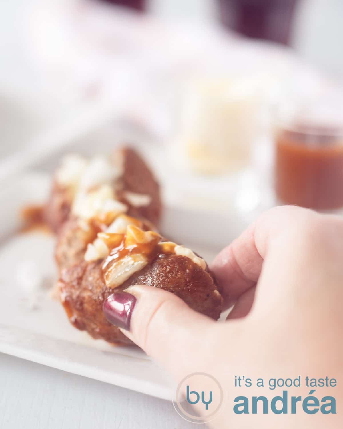 Een hand die een stukje afbreekt van een frikandel speciaal. Wat sausjes op de achtergrond