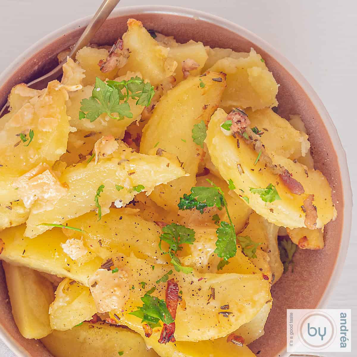 Een vierkante foto met geroosterde knoflookaardappelen met spekjes, kruiden en Parmezaanse kaas