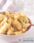 Een roze schaaltje met geroosterde knoflook aardappelen met kruiden. Twee glazen en een theedoek