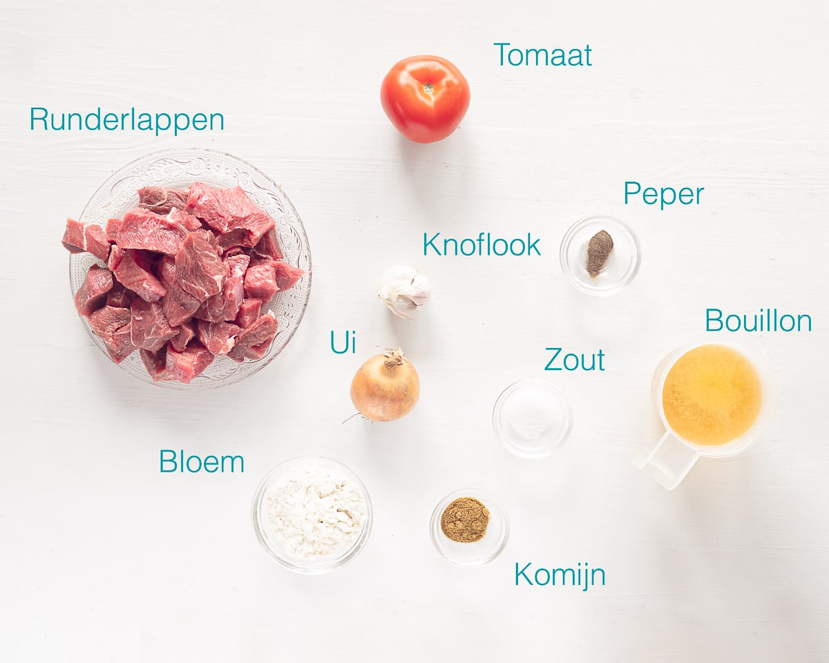 Ingrediënten Mexicaanse Carne Guisada op een witte ondergrond met de ingrediënten er in blauwe tekst bijgeschreven.