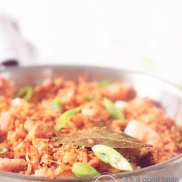 Een macro foto van een pan gevuld met Jambalaya rijst met garnalen, kip en worst. Garnerering met lente ui op een witte ondergrond