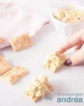 A hand grabbing a toast with chicken curry salad. A second piece of toast lies underneath. In the top left corner a pink white striped cloth and in the top right the rest of the salad