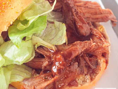 Een vierkante foto met daarop een broodje pulled pork en salade.