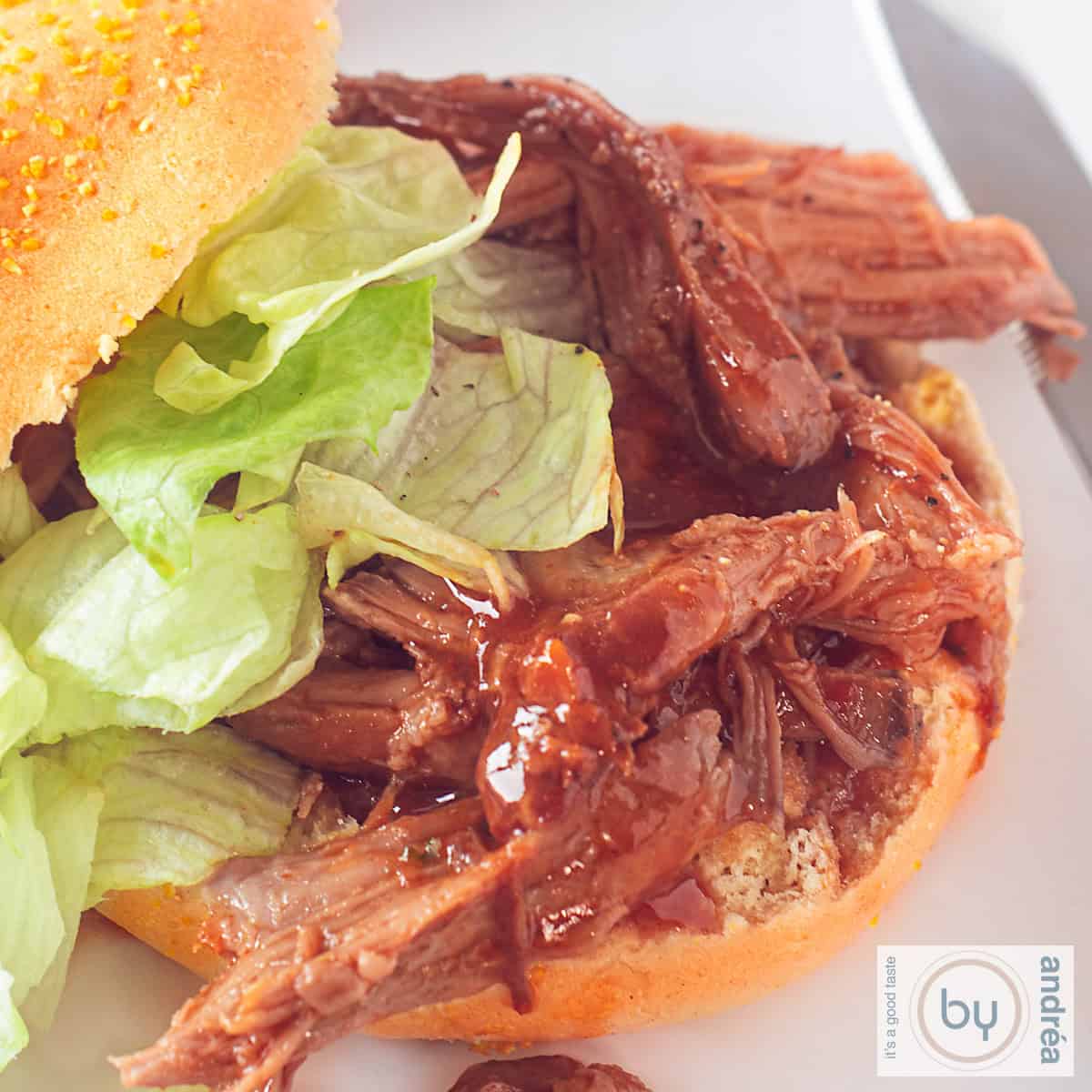 Een vierkante foto met daarop een broodje pulled pork en salade.