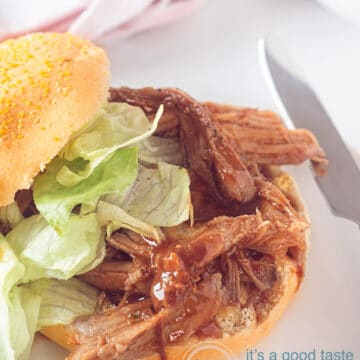 Een witte ondergrond, daarop een broodje met BBQ pulled pork en een salade. Een mes er rechts naast, een witte ondergrond