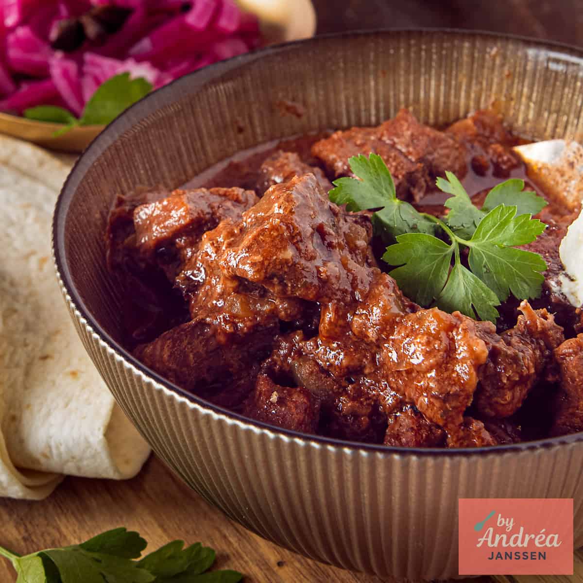 Een vierkante foto met Mexicaans stoofvlees in een kom, wraps en garnituur erbij.