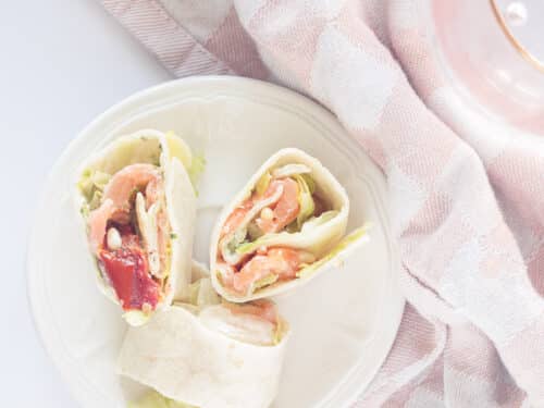 Drie heerlijke wraprolletjes met gerookte zalm en ijsbergsla op een zwart bordje op een zwarte ondergrond