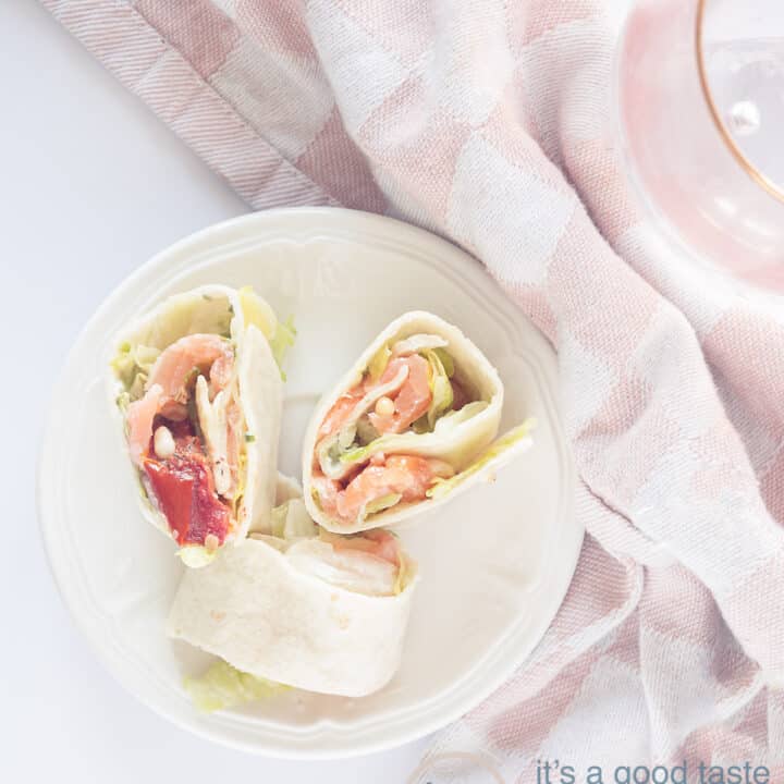 Drie heerlijke wraprolletjes met gerookte zalm en ijsbergsla op een zwart bordje op een zwarte ondergrond