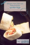 Drie wraps gevuld met gerookte zalm, Heksenkaas en ijsbergsla op een zwart bordje. Een text overlay beschrijft de foto.