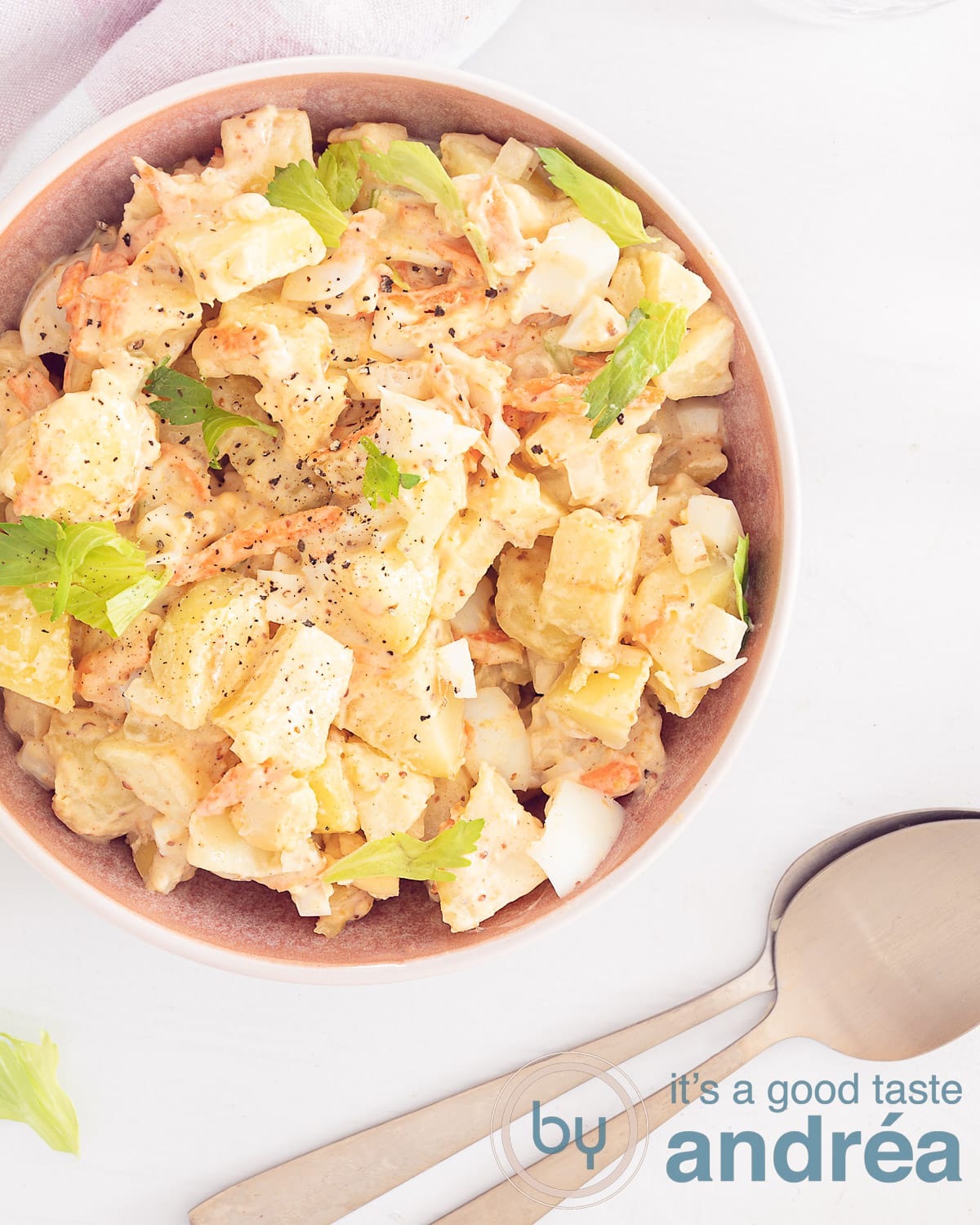 Foto van bovenaf van aardappelsalade met bleekselderij, ei, wortel en een romige dressing op een witte ondergrond