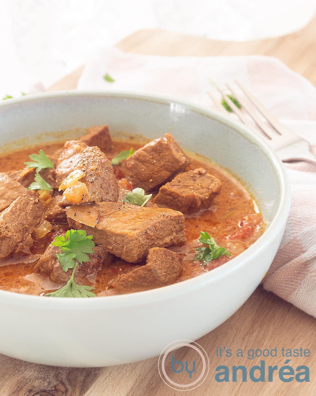 Een deel van een blauwe kom gevuld met Indiase curry Bombay gegarneerd met peterselie op een houten plank.