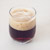 Een glas gevuld met bruin bier op een witte ondergrond