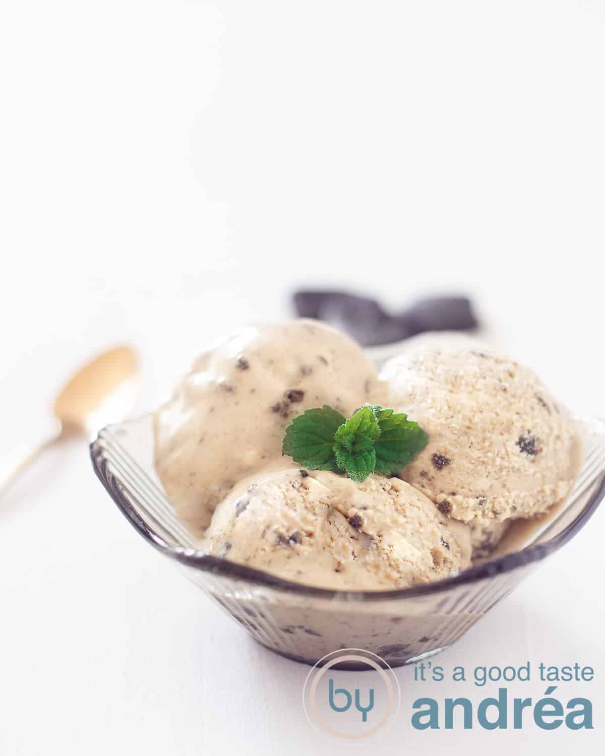 A bowl filled with ice cream with a liquorice flavour. Leaves of mint on the ice. A hand grabs a scoop of ice cream.