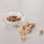 Pistachenoten gepeld in een glazen schaaltje, rechts liggen er wat naast op een witte ondergrond