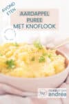 Een deel van een roze schaal op een witte roze theedoek met aardappelpuree met knoflook en sjalotjes. Peterselie gegarneerd. Een tekstoverlay bovenin: aardappelpuree met knoflook, avondeten, makkelijk recept, smaakvol