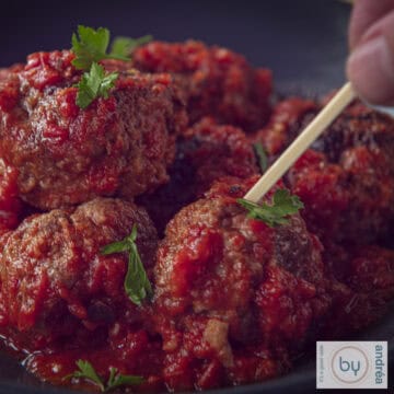 Een vierkante foto met gehaktballetjes in tomatensaus, Spaans. Een prikker prikt in een balletje