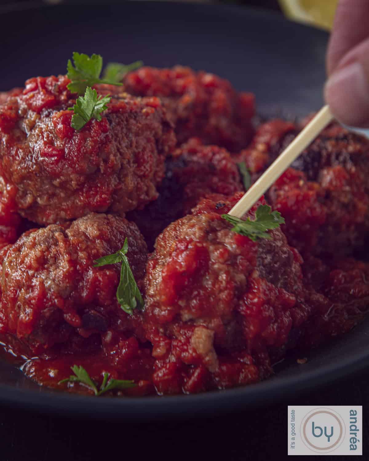 Albondigas in een donker schaaltje. Een prikker prikt een gehaktbal.