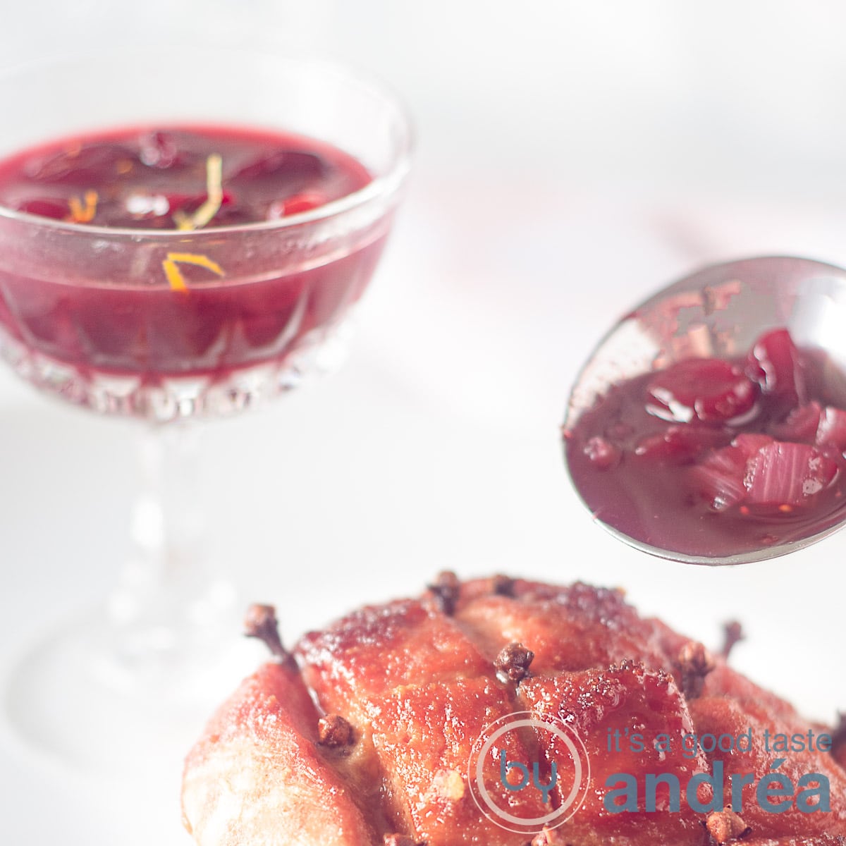 Een glas cumberlandsaus en een sauslepel gevuld met saus op een witte ondergrond. Onderin is nog een stuk beenham te zien.