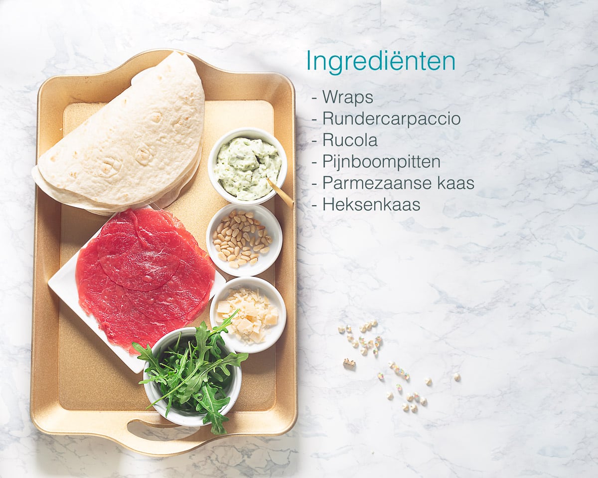 Ingrediënten zelf carpaccio wraps maken met heksenkaas op een gouden dienblad links, aan de rechterzijde een opsomming van de ingrediënten in tekst.