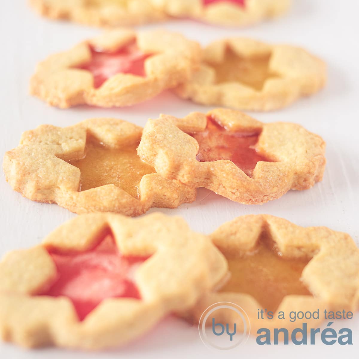 Een vierkante foto met zes koekjes gevuld met zuurtjes zodat ze lijken op glas in lood. Twee aan twee (rood en gele vulling) boven elkaar op een witte ondergrond.