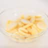 Een glazen kom gevuld met plakjes aardappels op een witte achtergrond