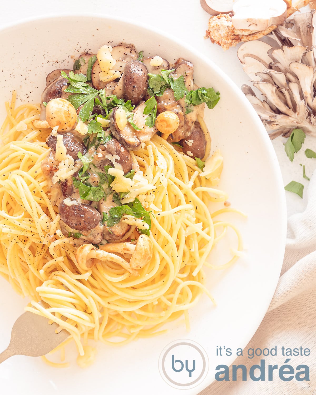 Een foto van bovenaf met rechtsbovenin een mix van verse champignons. Links een wit bord met spaghetti, gebakken champignons in een roomsaus.